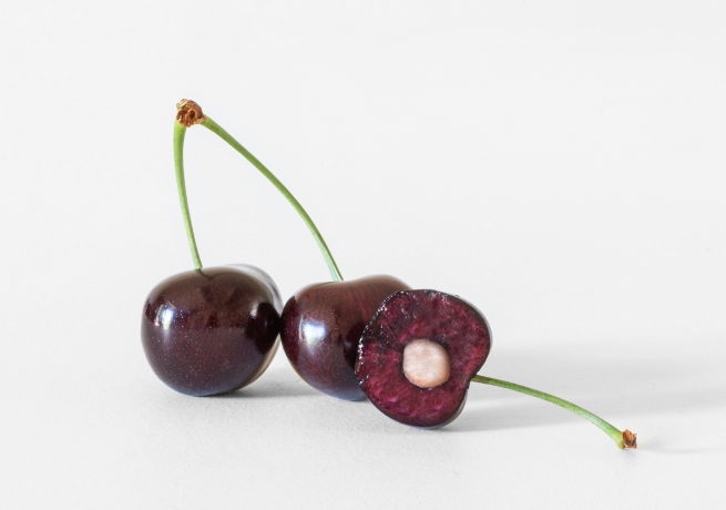 Trio of cherries with one split in half showing the seed on a white background